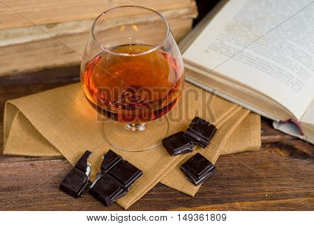 Glass of brandy and a chocolate on a old wooden table with old books
