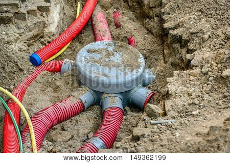 Hole in the ground with a grey covered junction of flexible plastic conduits not yet fastened hoses and cables.