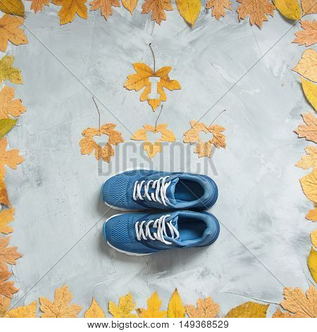 I love running composition with leaves and sport shoes on a concrete background. Concept running in autumn healthy life. Square orientation.