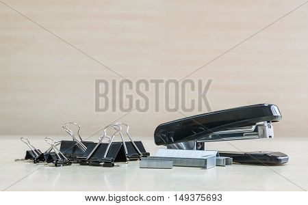 Closeup black stapler and black stamp paper clip office equipment on blurred wood desk and wall in office room textured background under window light