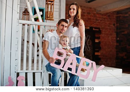 Young Caucasian Happy Family In Love Idoor Room With Letters Of The Word Baby