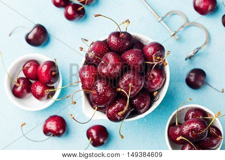 Fresh ripe black cherries in a white bowl on a blue stone background Top view.