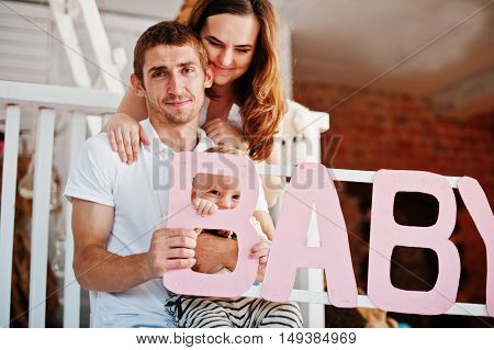 Young Caucasian Happy Family In Love Idoor Room With Letters Of The Word Baby