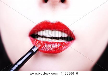 Fashion photo of face makeup demonstrating lips of a cute girl painted with bright lipstick with the hepl of brush.