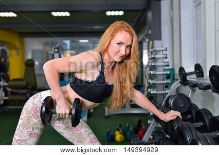 Fitness, sport, exercising lifestyle - Young woman doing heavy weight exercise for broadest muscle of back with dumbbells at gym.