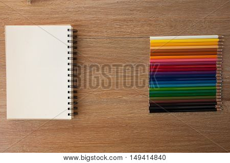 color pencils with notebook on wooden table