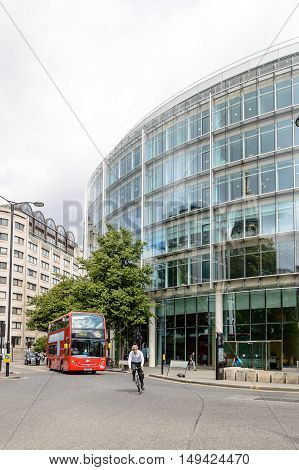 LONDON UK - AUGUST 21 2015: Cheapside street in London with a cyclist and a red bus. St. Pauls Cathedral is reflected on a modern glass facade.