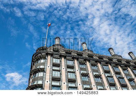 London UK - August 19 2015: Low angle view of Portcullis House in London with the Union Jack flag against blue sky and white clouds near Westminster Palace.