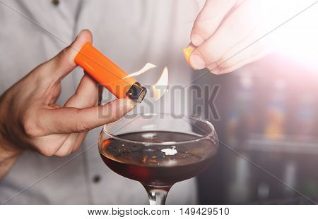 Barman's hands in bar interior making alcohol flaming cocktail. Professional bartender at work in bar mixing drink with burning fire. Party time in night club