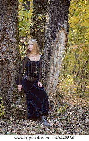 Blond Long-haired Girl In A Fantasy Black Dress In An Autumn Forest