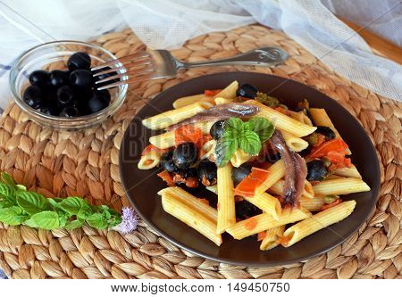 Delicious italian pasta penne with anchovies on a plate on a table.