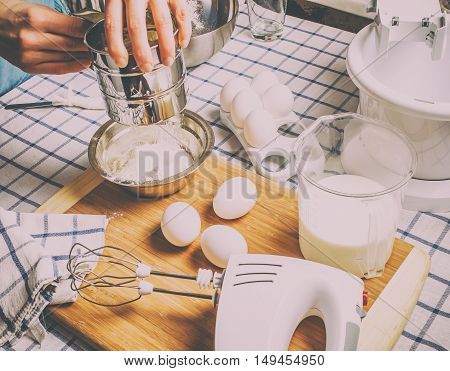 Sift flour man standing behind a table on which the chef prepared ingredients for a batch of pancakes and cake dough.