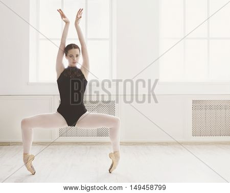 Classical Ballet dancer side view. Beautiful graceful ballerine in black practice ballet plie positions near large window in light hall. Ballet class training, high-key soft toning, copy space