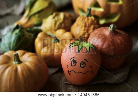 an apple disguised as a pumpkin with a funny face trying to go unnoticed between different real pumpkins