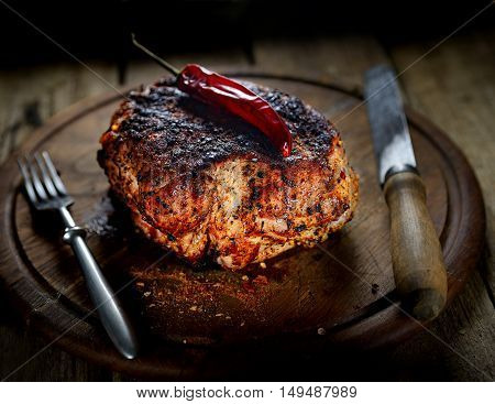 juicy piece of pork, pepper, noh and fork on a wooden background
