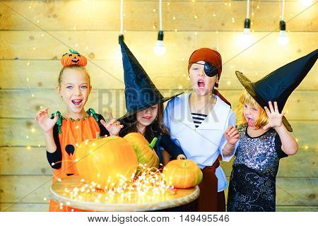 Happy group of witch children pirate and demons during Halloween party playing around the table with pumpkins