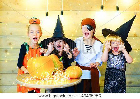 Happy group of witch children pirate and demons during Halloween party playing around the table with pumpkins