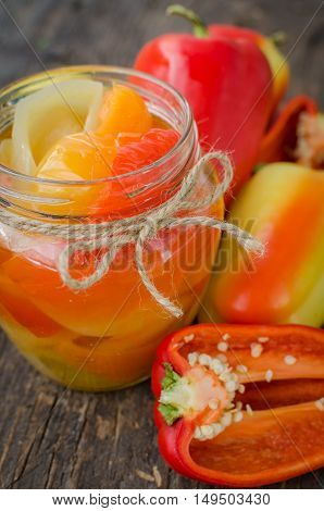 Bell pepper preserved in a glass jar with fresh peppers on old wooden background. Homemade marinated in oil red pepper. Glass jar with conserved roasted yellow and red paprika. Selective focus.
