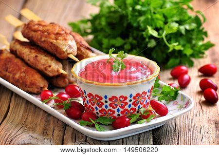 Homemade sauce dogberry with meat kebabs on wooden skewers.