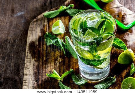 Glass of alcohol cocktail or lemonade. Mohito cocktail with lemon, lime, mint, ise cubes. Cold drink. Fresh lime and mint on wooden background