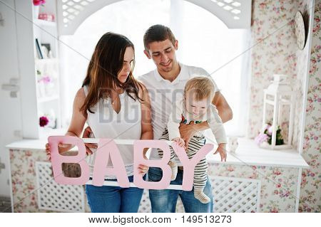 Young Caucasian Happy Family In Love Idoor Room With Letters Of The Word Baby