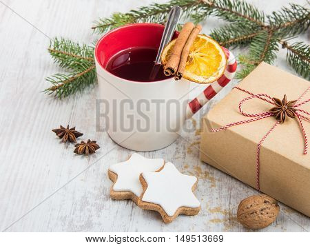 Homemade butter nuts star shaped cookies with icing pine orange slicescinnamon anise and walnuts over white wood background. A cup of berry tea and a gift box wrapped in kraft paper. Christmas decoration.