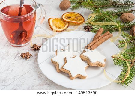 Close up of homemade butter nuts star shaped cookies with icing pine orange slicescinnamon anise walnuts and golden ribbon over white wood background. A cup of berry tea. Christmas decoration.