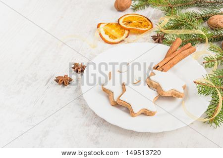 Close up of homemade butter nuts star shaped cookies with icing pine orange slicescinnamon anise walnuts and golden ribbon over white wood background. Christmas decoration.