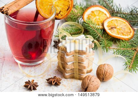 Homemade butter nuts star shaped cookies with icing pine orange slicescinnamon anise walnuts and golden ribbon over white wood background. A cup of berry tea. Christmas decoration.