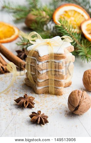 Close up of homemade butter nuts star shaped cookies with icing pine orange slicescinnamon anise walnuts and golden ribbon over white wood background. Christmas decoration.