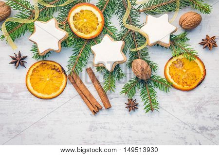 Christmas decoration over white wood background. Top view of homemade butter nuts star shaped cookies with icing pine orange slicescinnamon anise walnuts and white ribbon