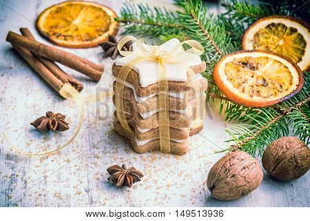 Close up of homemade butter nuts star shaped cookies with icing pine orange slicescinnamon anise walnuts and golden ribbon over white wood background. Christmas decoration.
