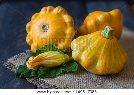 three yellow pattypan squash with leaf and flower on a dark wooden table.