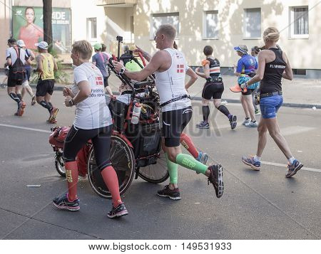 BERLIN GERMANY - SEPTEMBER 25 2016: Marathon runners run at Berlin Marathon 2016 in the city center of Berlin. One pushes a man in a wheelchair.