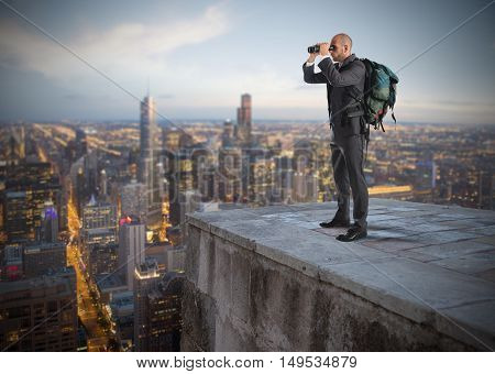 Businessman with backpack and binoculars watching from above the city