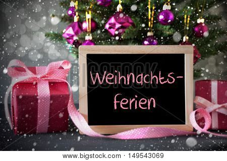 Chalkboard With German Text Weihnachtsferien Means Christmas Break. Christmas Tree With Rose Quartz Balls, Snowflakes And Bokeh Effect. Gifts Or Presents In The Front Of Cement Background.