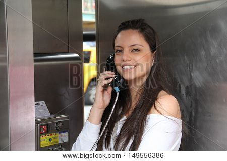 Happy pretty young girl talking by public telephone. Communication concept.