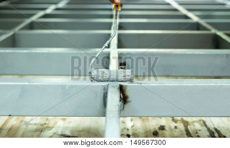 Worker painting steel bars with paintroller on construction site