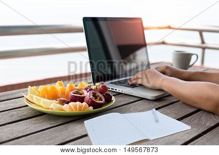 Selected focus fresh fruit with man working on laptop and notebook with pen with sunlight