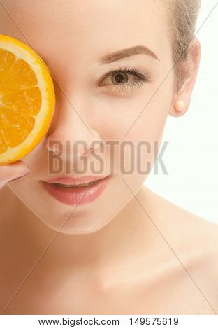 Face of a beautiful young woman who is holding a half of orange slices in front of his eyes and smiling. White background