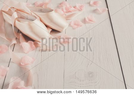 Pastel pink ballet shoes background. New pointe shoes with satin ribbon and rose petals lay on white rustic shubby chic wood, view with copy space, soft toning