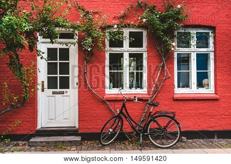 September, 23th, 2015 - Copenhagen, Denmark. Street, wall and bike. White color windows, door and modern bicycle leaned to red wall with blossom flowers.