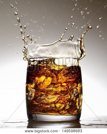 splash in a glass of whiskey and ice on gray background