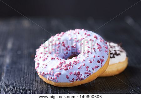 Close view at tasty donuts with blue and vanilla icing on a dark wooden background. Shallow depth of field