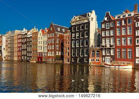 Beautiful typical Dutch dancing houses at the Amsterdam canal Damrak in sunny day, Holland, Netherlands.