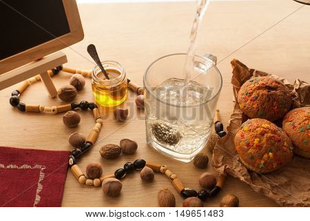 Preparing of chinese flower green tea with jasmine set with fresh just baked cupcakes made with chocolate and nuts. Falling hot boiled water into a cup with tea.