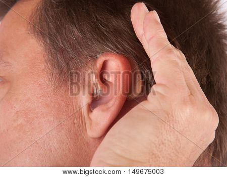 Close up of a man's ear with hearing aid. The deaf man cupping his hand behind his ear.
