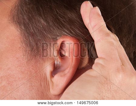 Close up of a man's ear with hearing aid. The deaf man cupping his hand behind his ear.