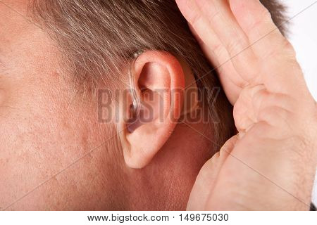 Ear of a man close up with hearing aid. The man is cupping his hand behind his ear.