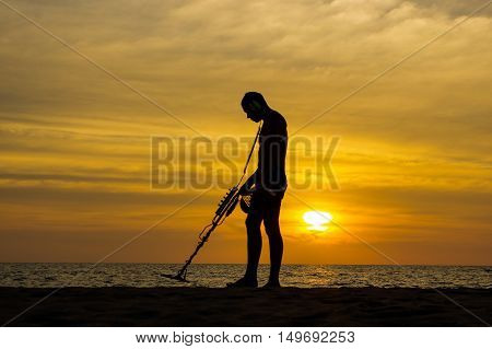 a treasure hunter with Metal detector on sunset on the beach